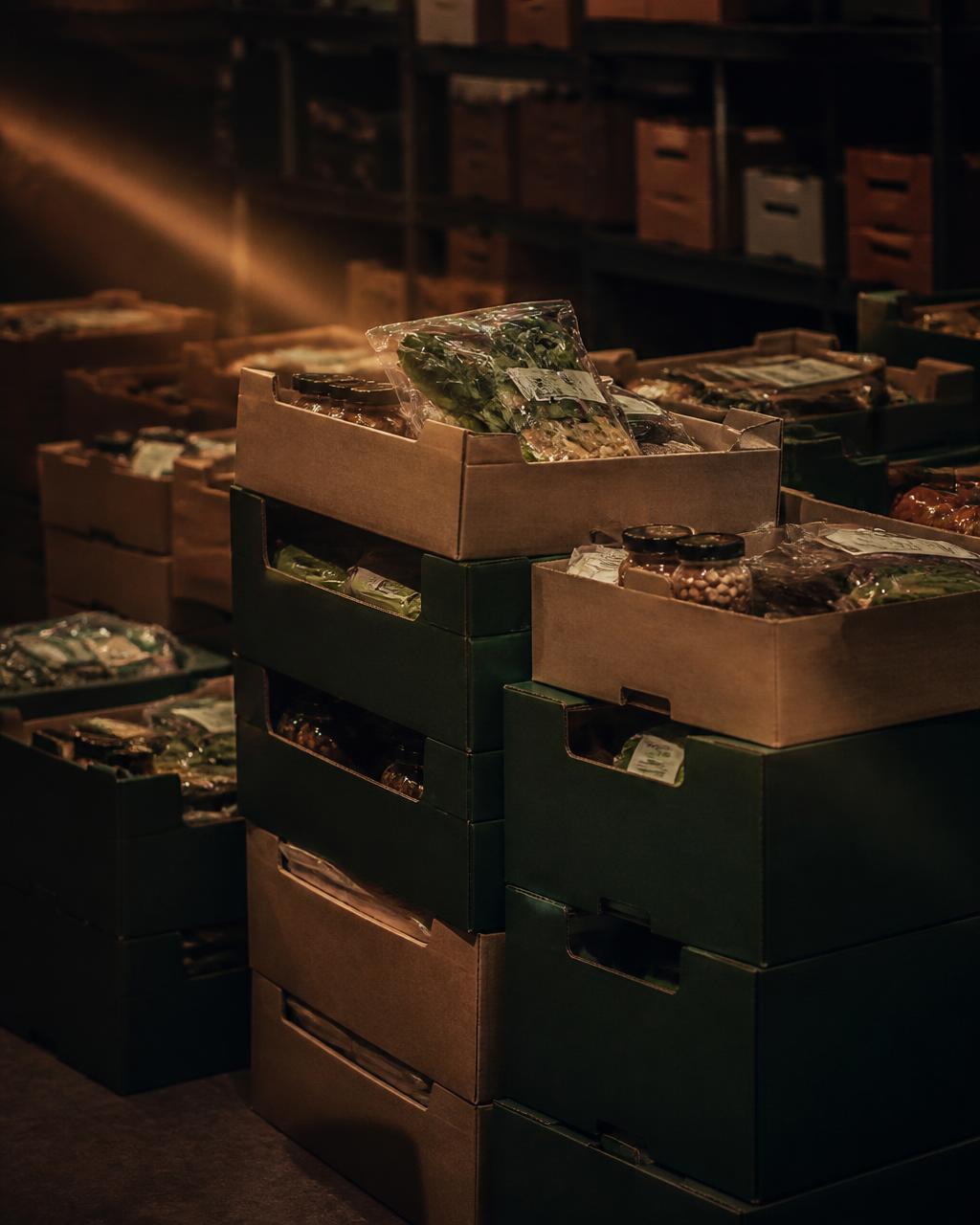 Crates of packaged fresh groceries stacked in a dim warehouse